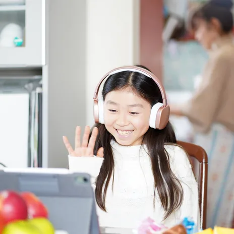 Smiling young girl wearing headphones attending an online language learning session at home


