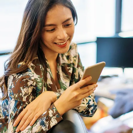 A woman in an office setting, smiling while using her phone, representing a modern approach to global corporate language training.