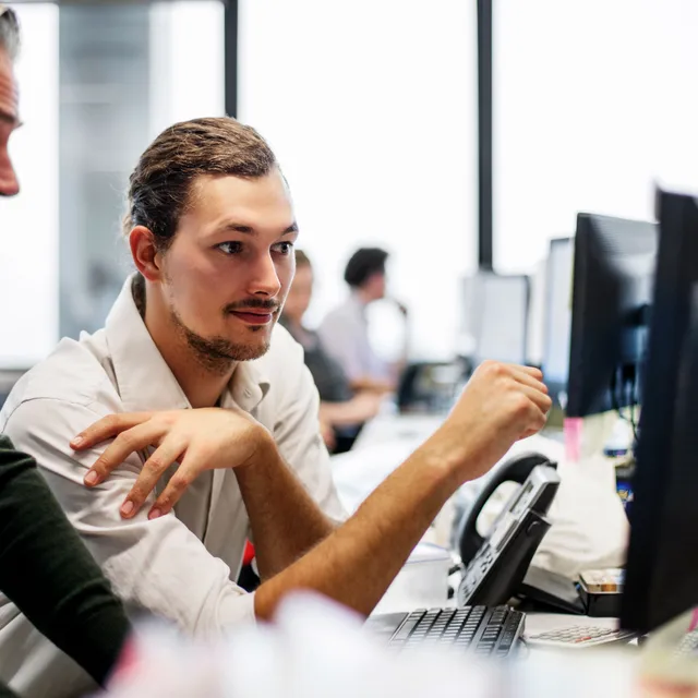 Two professionals reviewing Berlitz language proficiency test results on a computer in a modern office