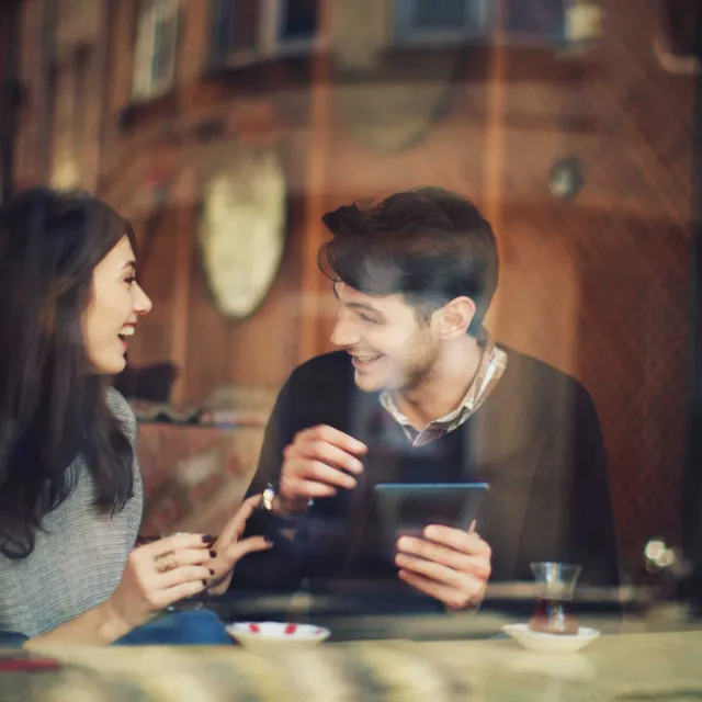 Man and woman enjoying a lively conversation at a café, illustrating real-life fluency through the immersive Berlitz Method.

