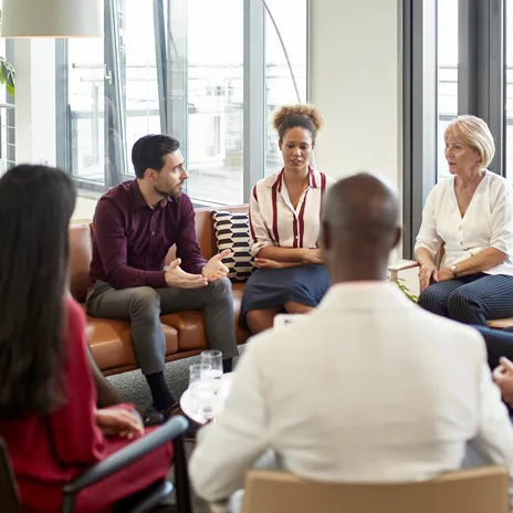 A diverse group of professionals engaged in a discussion in a modern office setting, representing language testing services for businesses and organizations.